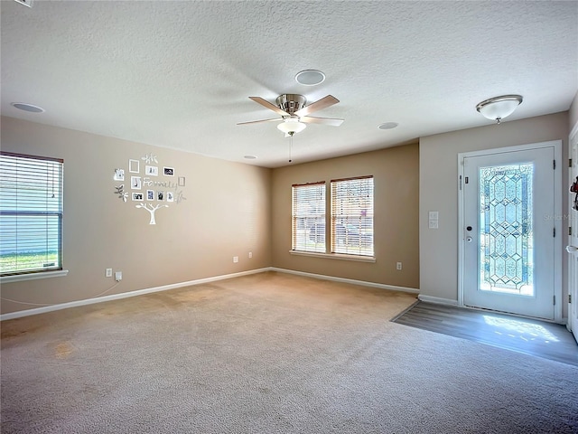 entrance foyer featuring a wealth of natural light, light colored carpet, baseboards, and a ceiling fan