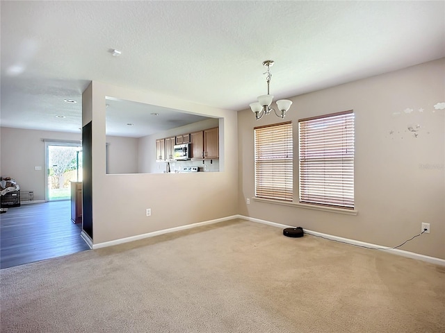 empty room featuring an inviting chandelier, baseboards, carpet floors, and a textured ceiling