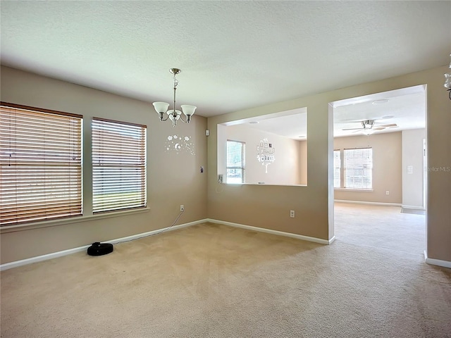 unfurnished room featuring ceiling fan with notable chandelier, light colored carpet, baseboards, and a textured ceiling