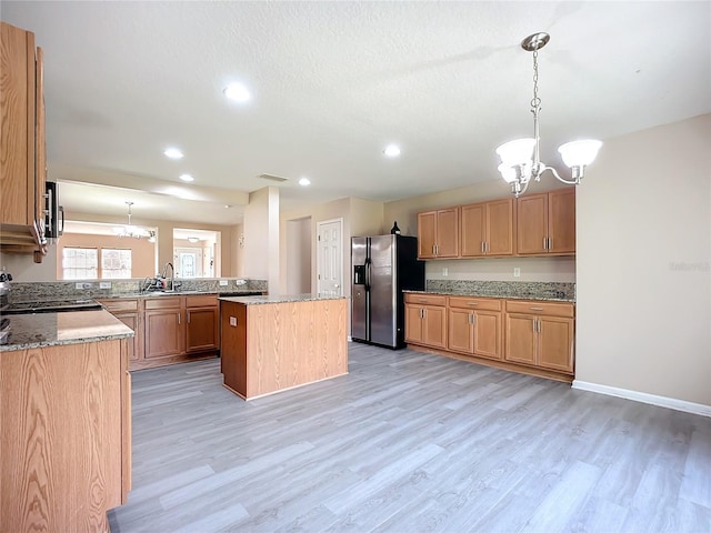 kitchen with light stone countertops, visible vents, light wood-style floors, stainless steel refrigerator with ice dispenser, and a notable chandelier