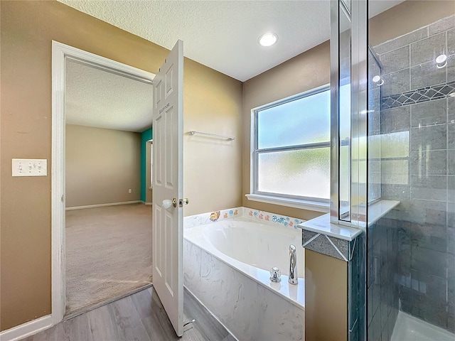 bathroom with baseboards, a textured ceiling, a bath, and a tile shower