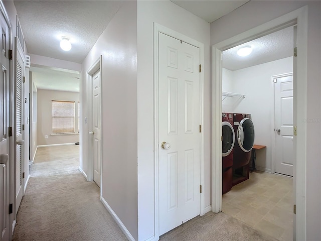 hall with washer and dryer, light carpet, baseboards, and a textured ceiling