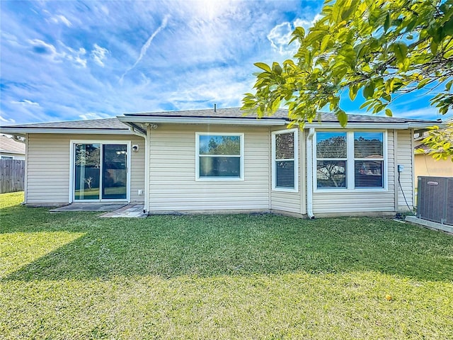 back of property with a lawn, central AC unit, and fence