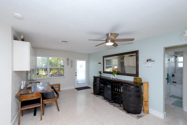 interior space with a ceiling fan, visible vents, baseboards, and speckled floor