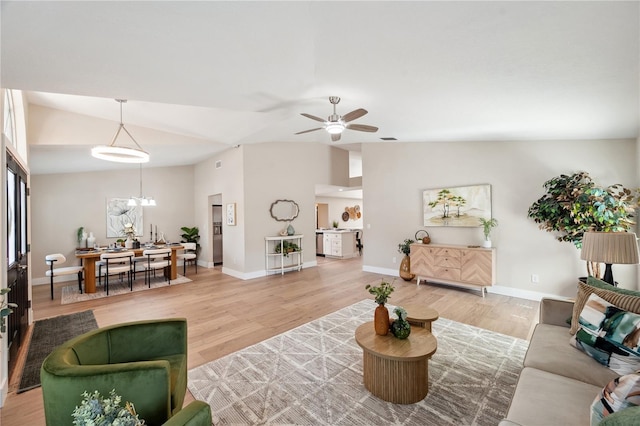 living room featuring light wood-style floors, vaulted ceiling, baseboards, and ceiling fan with notable chandelier