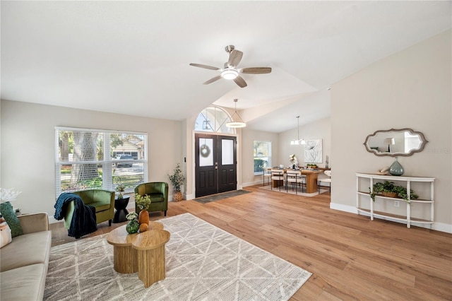 living room with lofted ceiling, light wood-style floors, baseboards, and ceiling fan with notable chandelier