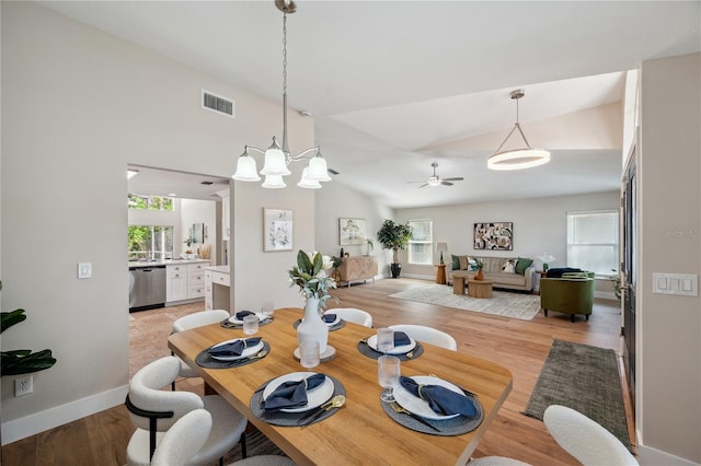 dining room featuring visible vents, light wood-style flooring, vaulted ceiling, baseboards, and ceiling fan with notable chandelier