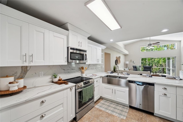 kitchen with appliances with stainless steel finishes, white cabinets, vaulted ceiling, and backsplash