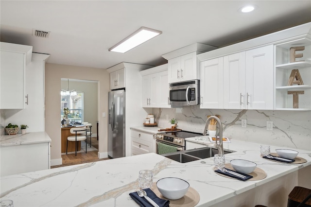 kitchen with stainless steel appliances, white cabinetry, a sink, and light stone countertops