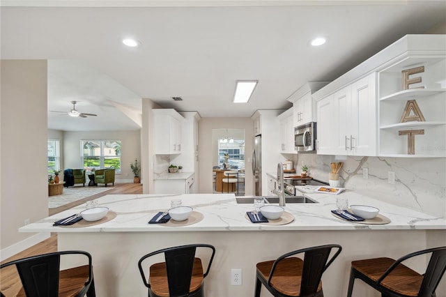 kitchen with white cabinets, light stone counters, a peninsula, stainless steel appliances, and open shelves