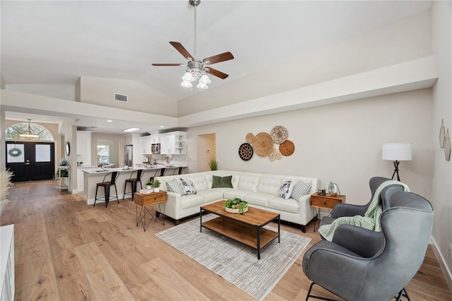 living area with lofted ceiling, light wood-style flooring, visible vents, and baseboards