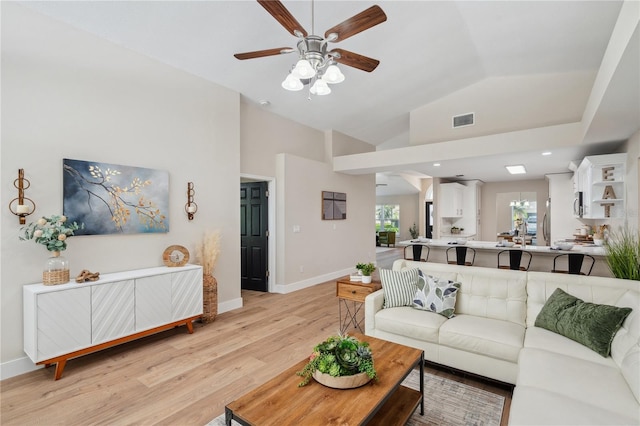 living room featuring ceiling fan, high vaulted ceiling, visible vents, baseboards, and light wood-type flooring