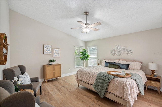 bedroom featuring vaulted ceiling, a textured ceiling, baseboards, and light wood-style floors