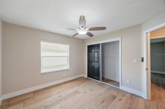 unfurnished bedroom featuring baseboards, a ceiling fan, light wood-style flooring, a textured ceiling, and a closet