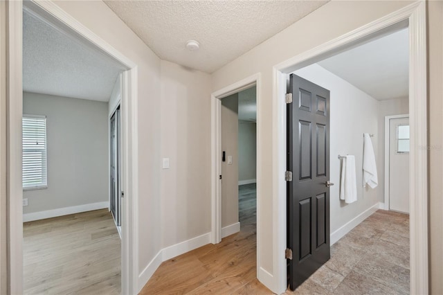 corridor with light wood finished floors, baseboards, and a textured ceiling