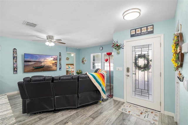 living room featuring a ceiling fan, visible vents, baseboards, and wood finished floors