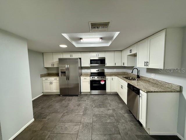 kitchen with stainless steel appliances, visible vents, white cabinetry, a sink, and dark stone counters