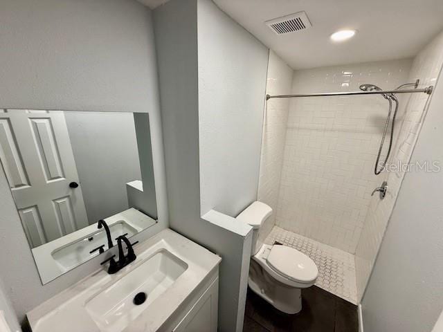 bathroom with visible vents, vanity, toilet, and tiled shower