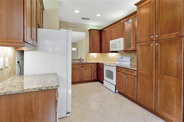 kitchen featuring visible vents, brown cabinetry, glass insert cabinets, light stone countertops, and white appliances