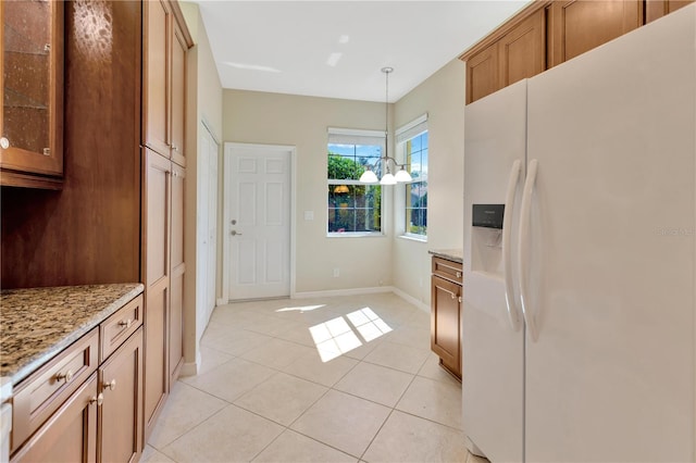 kitchen with white refrigerator with ice dispenser, glass insert cabinets, brown cabinets, light stone countertops, and light tile patterned flooring