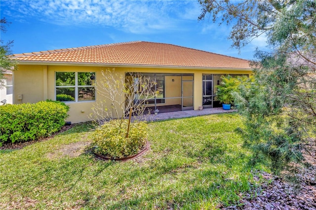 rear view of house with stucco siding, a tiled roof, a sunroom, and a yard