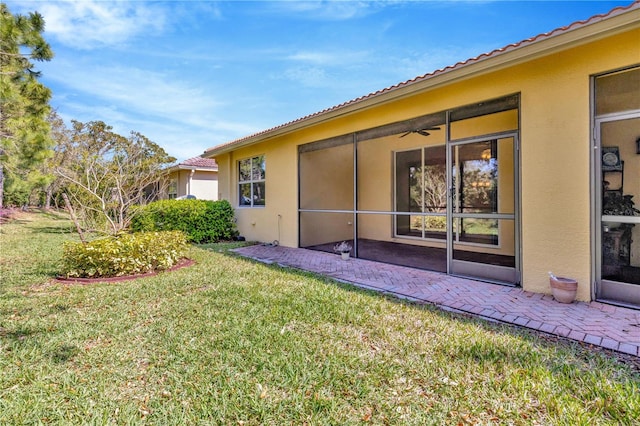 back of property with a sunroom, a patio area, a lawn, and stucco siding