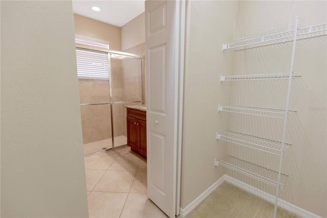 bathroom featuring tile patterned flooring, baseboards, a shower stall, and vanity