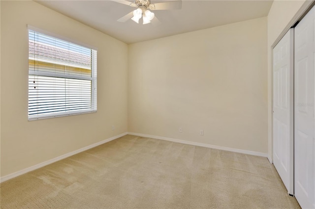 unfurnished bedroom featuring light carpet, a ceiling fan, baseboards, and a closet