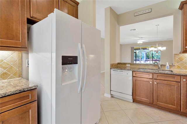 16232 Amethyst Key Dr, Wimauma, FL 33598 - kitchen with white appliances, brown cabinetry, decorative backsplash, light tile patterned floors, and light stone countertops