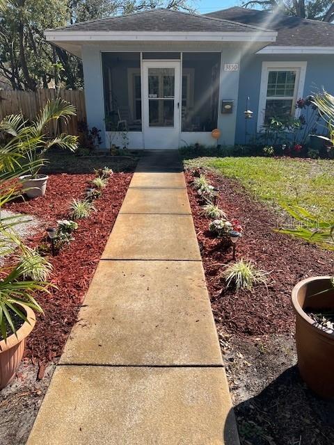 property entrance with a shingled roof, fence, and stucco siding