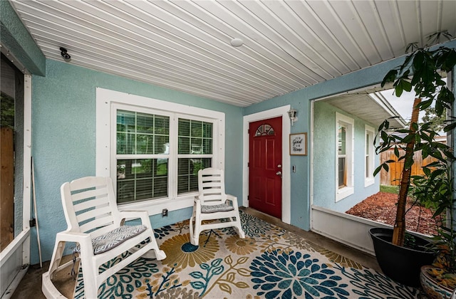 doorway to property featuring stucco siding, a porch, and fence