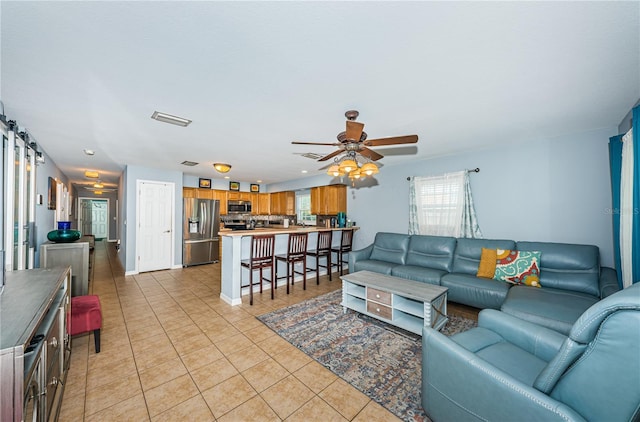 living room with light tile patterned floors, visible vents, a barn door, and a ceiling fan