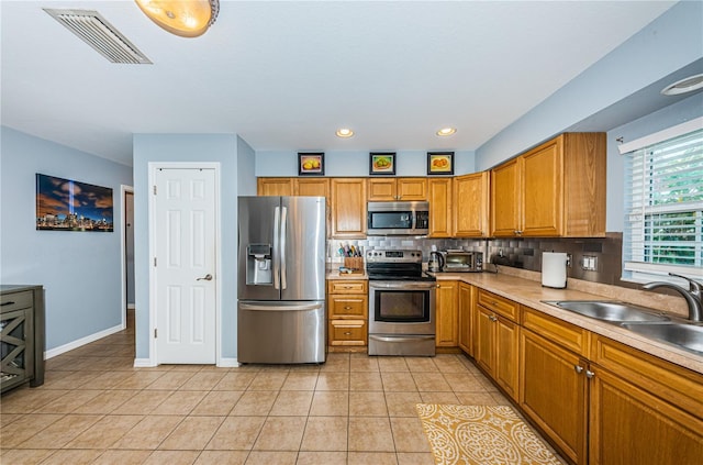 kitchen featuring visible vents, brown cabinets, a sink, backsplash, and stainless steel appliances