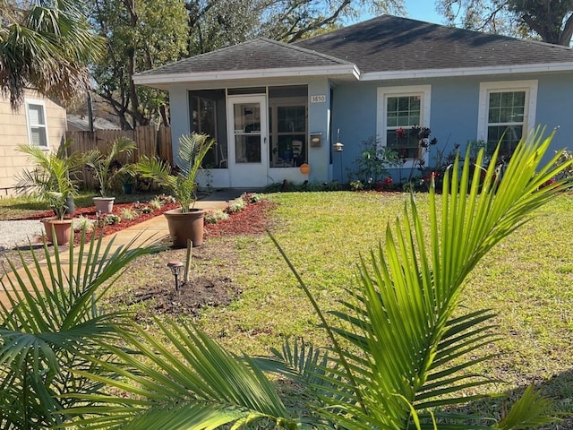 view of front facade with fence, a sunroom, a shingled roof, stucco siding, and a front lawn