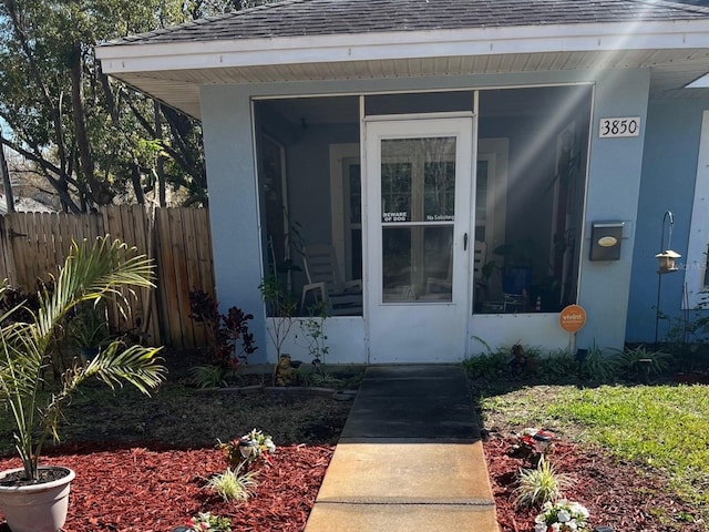 property entrance featuring stucco siding, fence, and a shingled roof