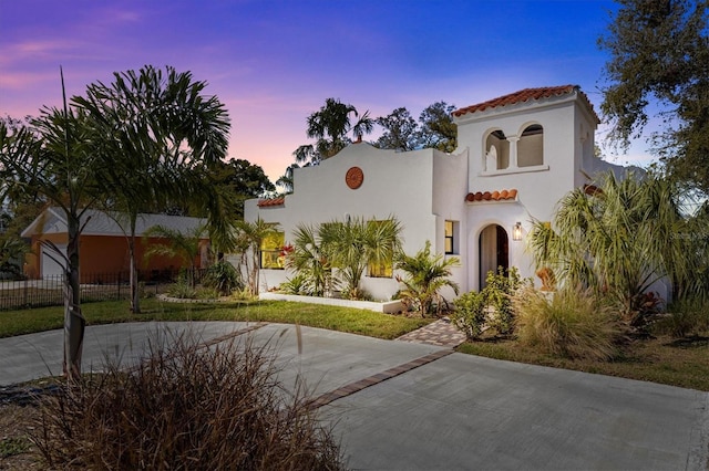 mediterranean / spanish house featuring concrete driveway, a tile roof, fence, and stucco siding