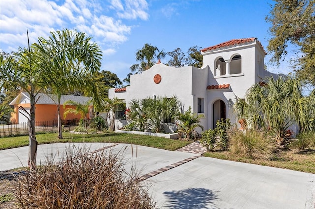 mediterranean / spanish-style house with a tiled roof, fence, and stucco siding