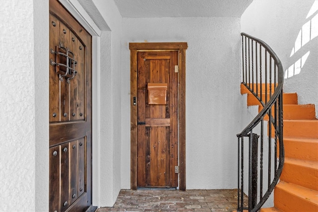 foyer entrance with brick floor, stairway, and a textured wall