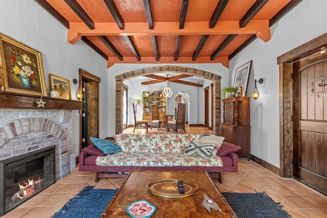 living area featuring arched walkways, vaulted ceiling with beams, light tile patterned flooring, baseboards, and a brick fireplace