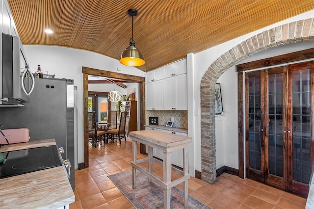 kitchen featuring baseboards, lofted ceiling, stainless steel microwave, decorative light fixtures, and white cabinetry