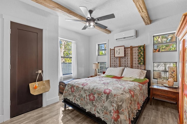 bedroom featuring a wall unit AC, beamed ceiling, light wood-style flooring, and multiple windows