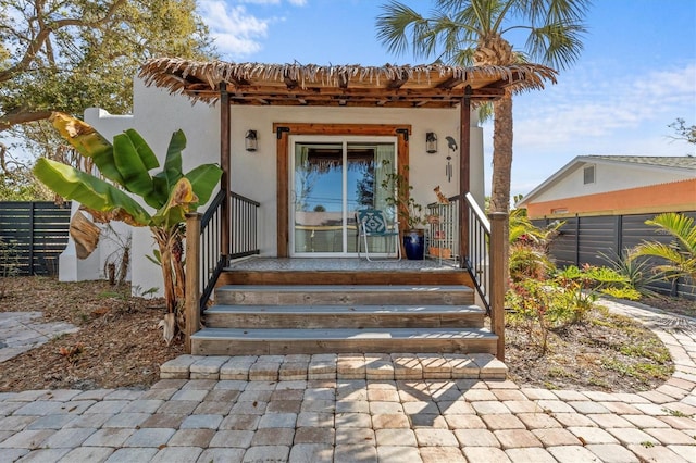 view of exterior entry featuring covered porch, fence, and stucco siding