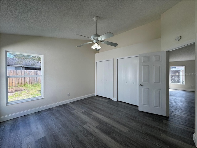 unfurnished bedroom with a textured ceiling, baseboards, dark wood-style flooring, and two closets