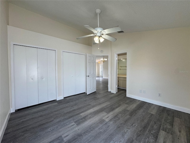 unfurnished bedroom featuring dark wood finished floors, two closets, vaulted ceiling, a textured ceiling, and baseboards