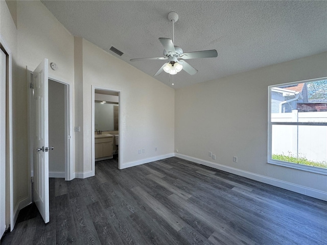 unfurnished bedroom featuring dark wood-style flooring, visible vents, vaulted ceiling, a textured ceiling, and baseboards