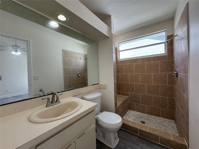 bathroom featuring a ceiling fan, tiled shower, vanity, and toilet