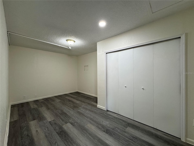 unfurnished bedroom featuring a textured ceiling, dark wood-type flooring, a closet, and baseboards