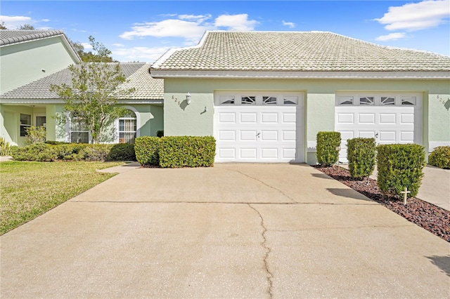 ranch-style home with a garage, a tiled roof, concrete driveway, stucco siding, and a front lawn