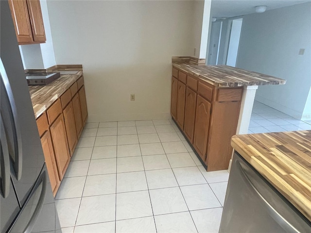 kitchen featuring light tile patterned floors, brown cabinetry, freestanding refrigerator, a peninsula, and wooden counters