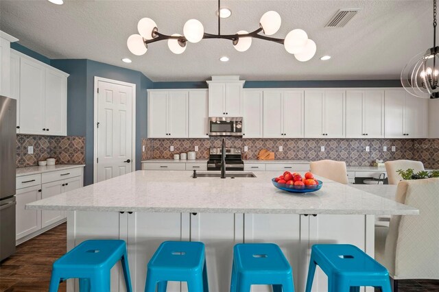 kitchen with stainless steel appliances, visible vents, an inviting chandelier, white cabinets, and a sink